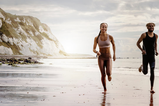 Young male and female runners running barefoot on beach