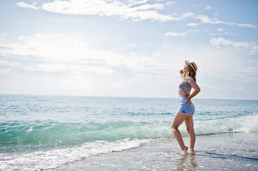 Beautiful model relaxing on a beach of sea, wearing on jeans short, leopard shirt and hat.