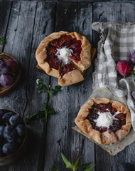plum crostata pies with ice cream on gray wooden table with textile, fresh plums and herbs