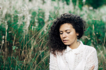 curly brunette on grass background. Amazing appearance of the girl. Autumn Portrait