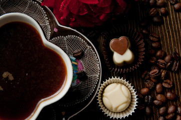 Cup of tea on a wood table near a rose and chocolate pralines lots coffee beans