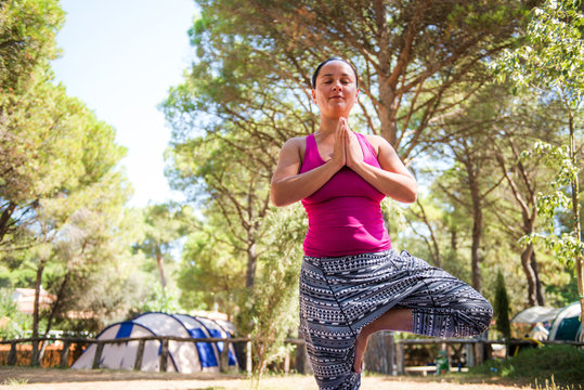 Mature woman practicing yoga tree pose on camping site