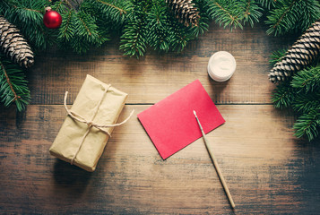 Christmas gift box, empty red card for your text, a brush and white paint, glass spheres, a Christmas fir-tree on a wooden background, top view. Christmas background