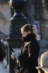 blonde woman with gloves leaning against a bridge looking at cell phone