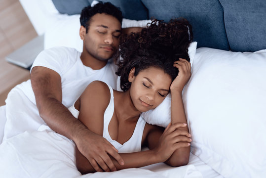 Black Man And Woman In The Bedroom. A Woman Is Lying In Bed And Her Man Is Hugging Her. They Sleep Embracing Each Other.