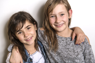 Two happy kids sister standing at blank grey wall and embracing