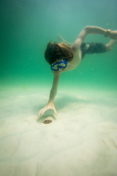 Teenage boy swimming underwater, reaching for shell on sea bed