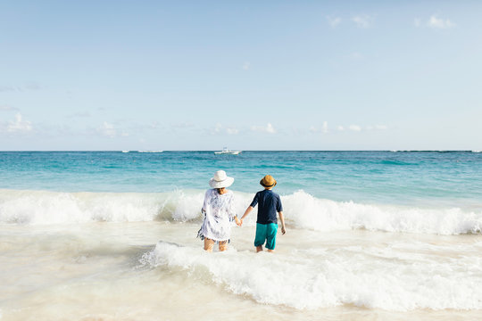 Mother and son, holding hands, standing in surf on beach, rear view