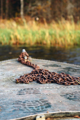 Old boat with a rusty chain and a boot trace on an autumn river