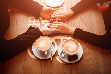 hand girl in a man's at the table with cups of coffee in the foreground