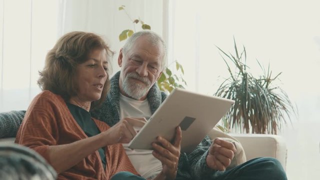 Senior couple with tablet relaxing at home.