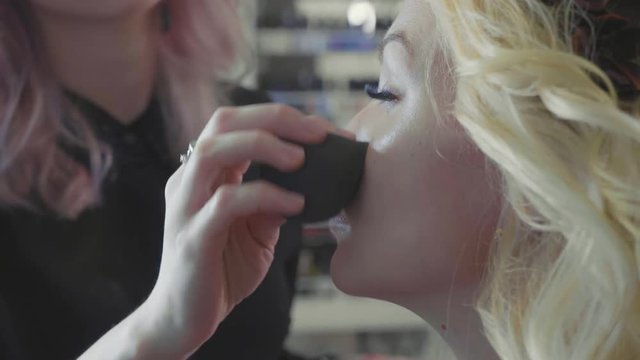 Young makeup artist applying concealer on model's face.