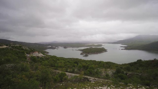Panning shot of mountain lake with small islend under overcast sky