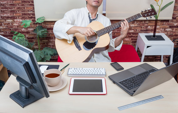 asian businessman playing guitar for relaxation between hard working in office