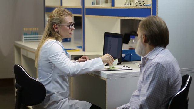 Doctor writing prescription to patient at hospital