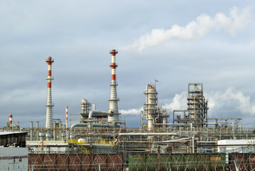 general view of a chemical or oil refinery with a multitude of pipelines, factory pipes, distillation columns and freight cars in the foreground under a cloudy sky
