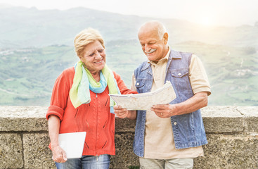 Senior couple reading tourist map inside italian castle outdoor - Mature Husband and wife having fun in romantic vacation - Love and joyful elderly lifestyle concept