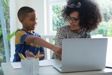 Son doing homework while mother using laptop 