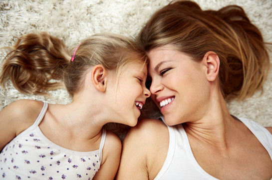 Pretty smiling girl with her mother lying on the floor and looking at each other in happiness. 