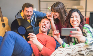 Obraz premium Happy friends taking selfie photo with smartphone camera at hostel party - Young people drinking and having fun together - Focus on left woman face - Friendship, music and gathering concept