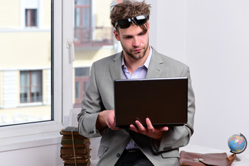 Businessman with laptop and pile of books on window background