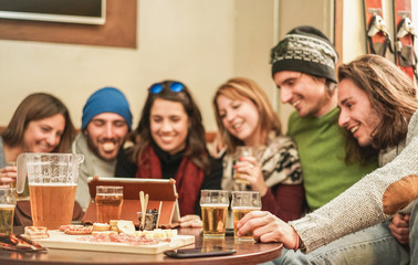 Happy friends watching videos and drinking beer at chalet pub in mountains - Young people having fun in winter vacation - Friendship concept - Focus on right man left hand - Warm filter
