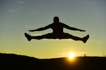 Silhouette of athlete jumping on sunset background, copy space.