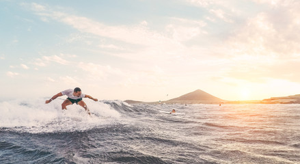 Fit athlete surfing at sunset - Surfer man performing outdoor inside ocean- Extreme sport and vacation concept - Soft focus on man - Contrast sun color tones filter