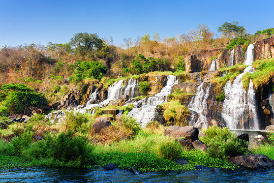 Fototapeta Kaskadowy wodospad wśród skał i roślinności ścienna