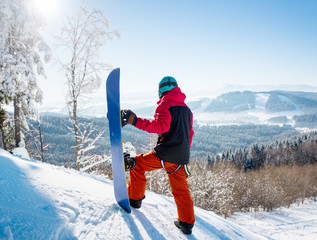 Rear view of snowboarder standing on top of a slope looking around enjoying the view at winter ski...