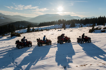 Group of people enjoying sunset, riding on quad bikes on snow in the the mountains in winter