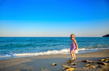 little beautiful girl in a dress and sunglasses, running and having fun on the beach.
