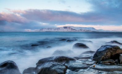 Winter view of the mountains from the promenade. Reykjavik, Iceland. Coastline wet stones, washed by waves at sunset.