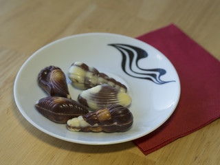 five close up chocholate nougat sea fruit shell on white plate red napkin on wooden desk dessert
