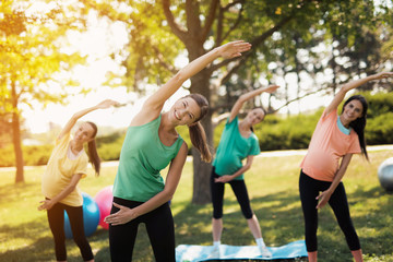Pregnancy yoga. Three pregnant women standing in the park and doing exercises. Together with them their coach