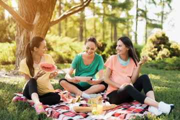 Three pregnant women rest on nature after doing yoga. One of them holds a tablet