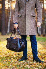 Clous up of the man in a coat and a leather bag in the beautiful autumn wood