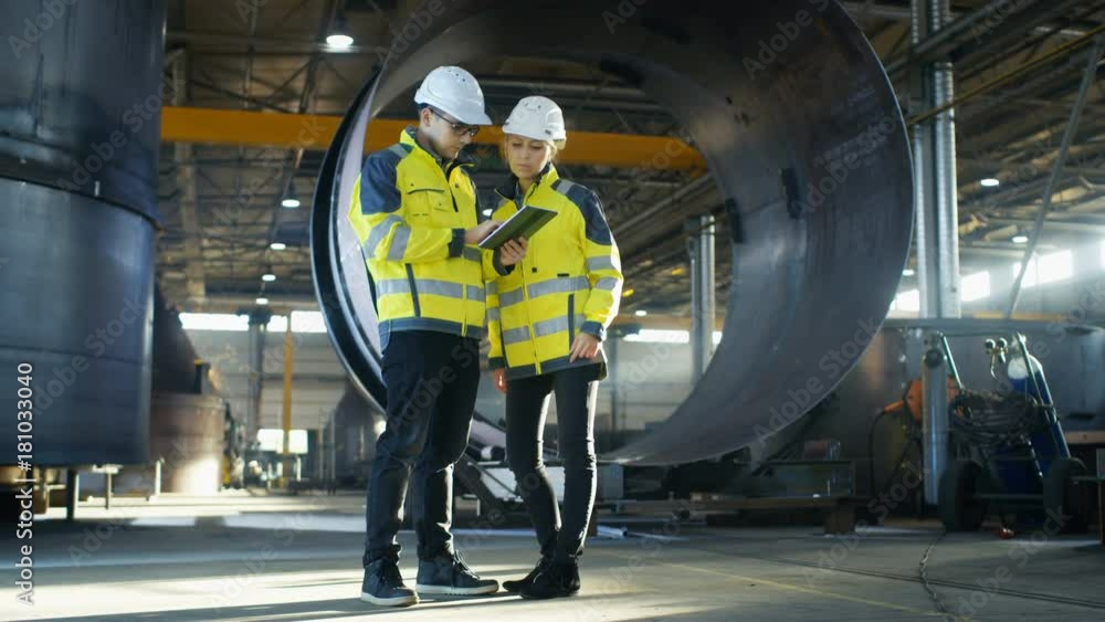 Poster male and female industrial engineers in hard hats discuss new project while using tablet computer. t