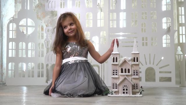 A kind girl in a gray dress with sparkles smiles and holds a toy palace, slow motion