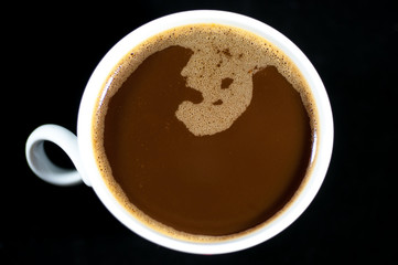 White cup of coffee isolated on black background, filled with milky coffee.