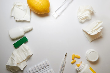 The concept of the common cold. used crumpled napkins, nasal drops, a blister with pills, a jar with yellow pills, a thermometer, a lemon and a ginger root. A frame of objects in the center white
