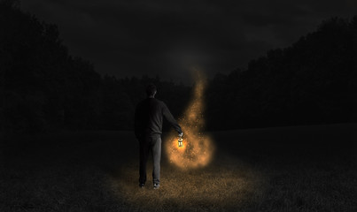 Man holding a lamp and following the fireflies at dark night.  Young man in deep forest in magical situation at night with light and old lamp. Old lamp and misty light effect.  Man silhouette in dark. - obrazy, fototapety, plakaty