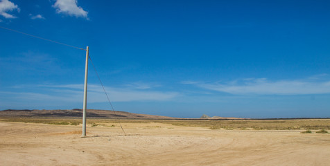 einzelner Strommast in Wüste mit blauen Himmel und kleinen Wolken