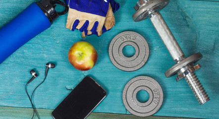 Weight plates, gloves and smartphone on wooden background