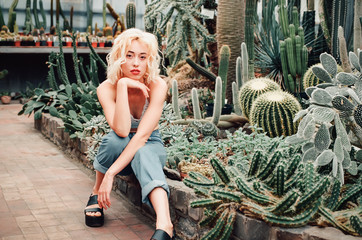 Young woman with blond hair walking between cactus and succulent plants in beautiful  tropical...