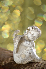 kleiner weißer Engel sitzt auf einem Brett aus Holz mit bokeh aus lichtern im hintergrund