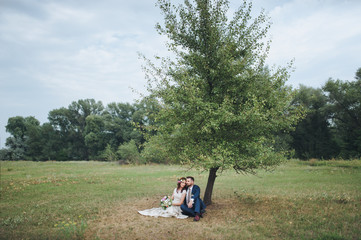 Fototapeta na wymiar The bride and groom are sitting on the grass under a tree. Lovers embrace in nature.