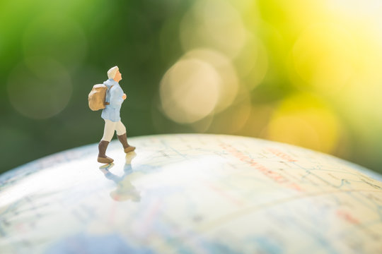 Travel Concept. Traveller miniature figure with backpack walking on world balloon with green nature as background.