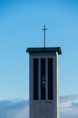 Church spire with cross on top of the roof and blue sky in background