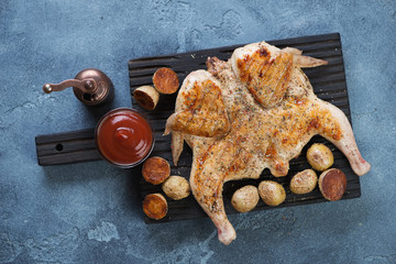 Black wooden serving board with chicken tabaka, fried cherry potato and sauce, flat-lay, studio shot